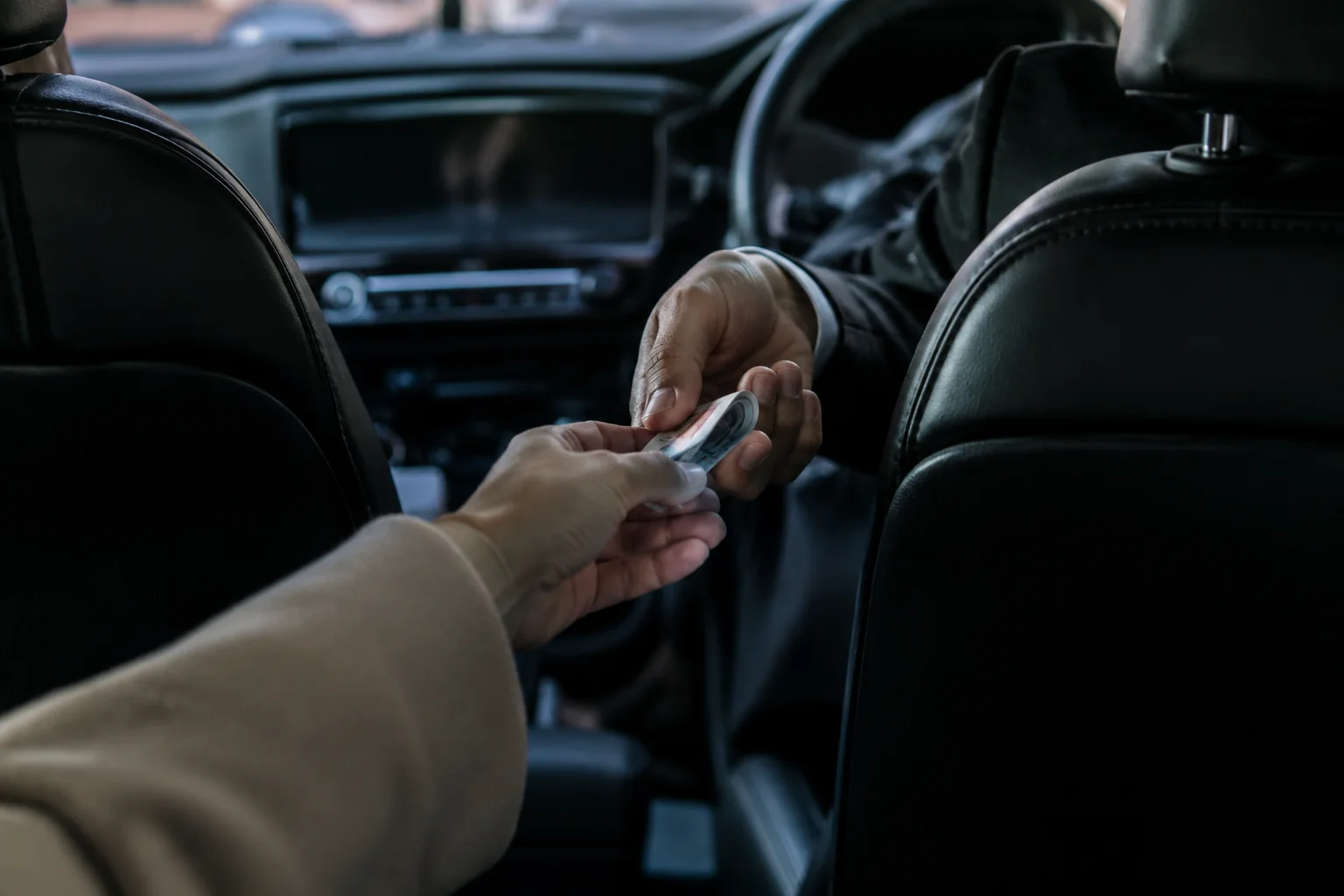 A passenger handing a note directly to the chauffeur at the end of a journey